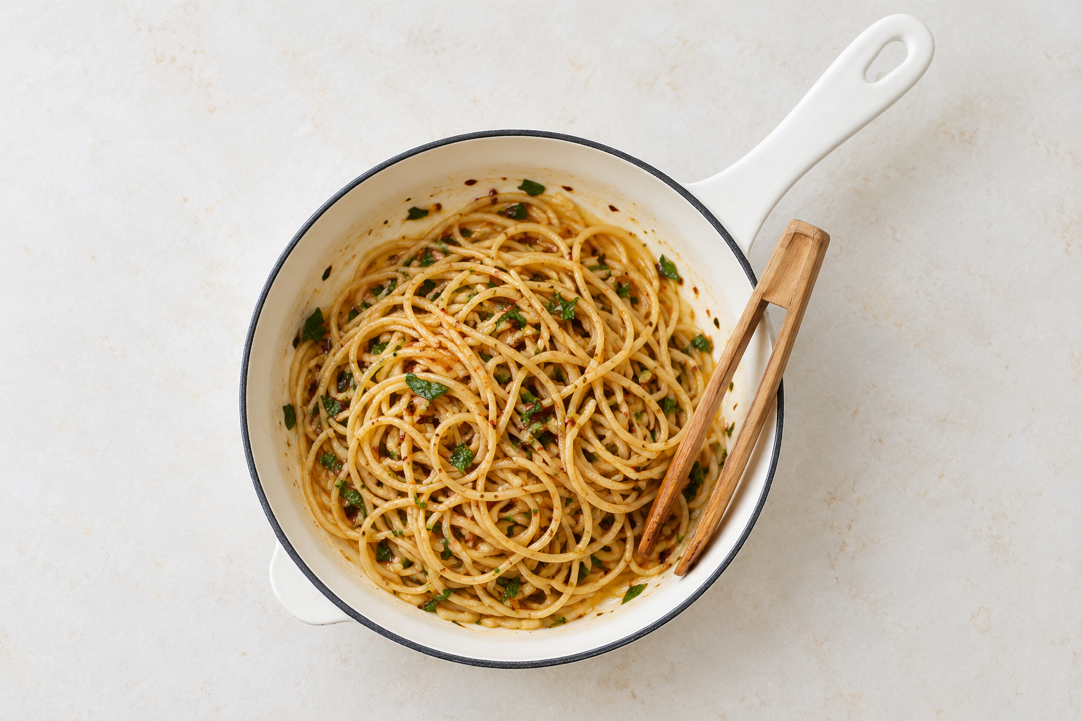 Overhead white pan of thin whole-grain spaghetti with minced garlic, chopped herbs and a light Rosso coating.
